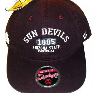May include: A maroon baseball cap with white embroidery that reads "Sun Devils 1885 Arizona State Phoenix, AZ". The cap has a black and white label that reads "Authentic Zephyr" with a white "Z" logo.