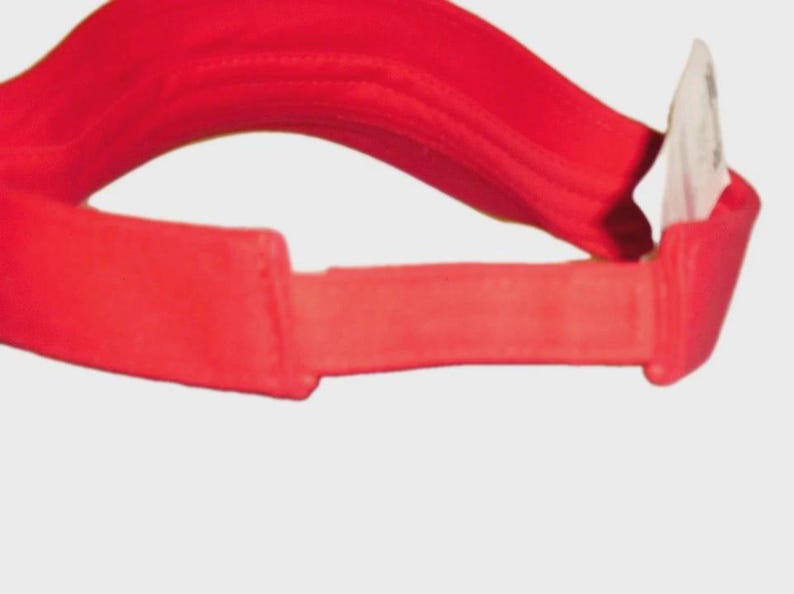 May include: A bright red visor, designed to shield the eyes from the sun. The visor features a curved brim and an adjustable strap. The material appears to be a lightweight fabric, suitable for outdoor activities. A white tag is attached.