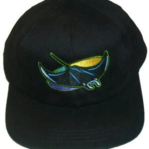 May include: Black baseball cap with an embroidered manta ray design in blue, green, yellow, and purple.