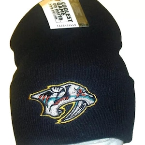 May include: Black knit beanie with a colorful embroidered Nashville Predators logo. The beanie has a tag that reads "Coolest Game on Earth".
