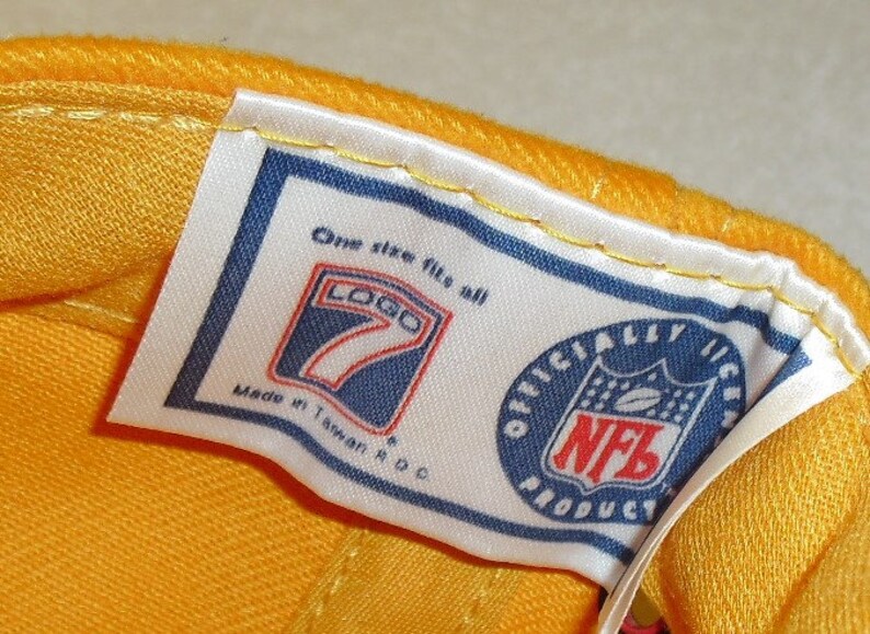 May include: A white tag with blue trim and text that reads "One size fits all" and "Logo 7" with a blue and white logo of the number 7. The tag also reads "Made in Taiwan, R.O.C." and "Officially Licensed NFL Product" with a blue and red NFL logo.
