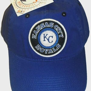 May include: A royal blue baseball cap with the Kansas City Royals logo. The logo is a circular patch with the team name and "KC" in the centre. A Major League Baseball merchandise tag is attached.