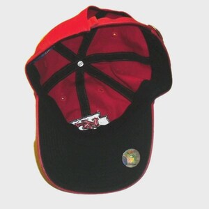 May include: A red baseball cap viewed from the inside, featuring black interior seam tape, a black brim underside, and a white embroidered logo patch. A circular NFL holographic sticker is affixed to the black brim, and a small Reebok logo tag is visible on the interior crown.