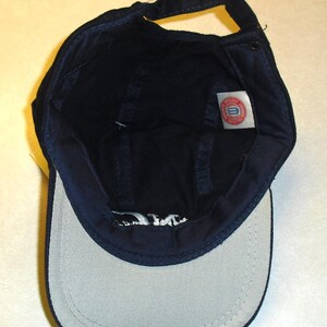 K&ouml;nnte beinhalten: Eine marineblaue Baseballkappe mit wei&szlig;em Schirm und einem rot-wei&szlig;-blauen Logo auf der Innenseite. Das Logo lautet "University of Delaware".