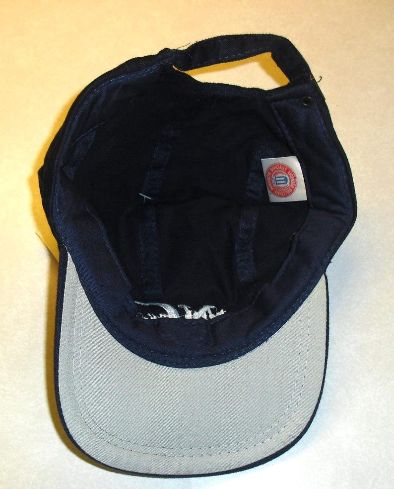 K&ouml;nnte beinhalten: Eine marineblaue Baseballkappe mit wei&szlig;em Schirm und einem rot-wei&szlig;-blauen Logo auf der Innenseite. Das Logo lautet "University of Delaware".