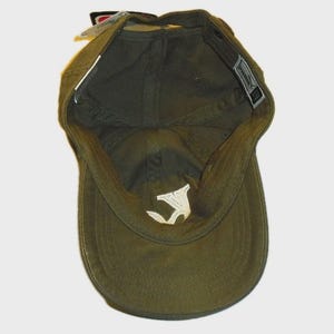 May include: An olive green baseball cap shown from an interior perspective, revealing the fabric lining, a white embroidered logo on the inner crown, and a rectangular brand tag attached to the inner seam near the back opening of the headwear.