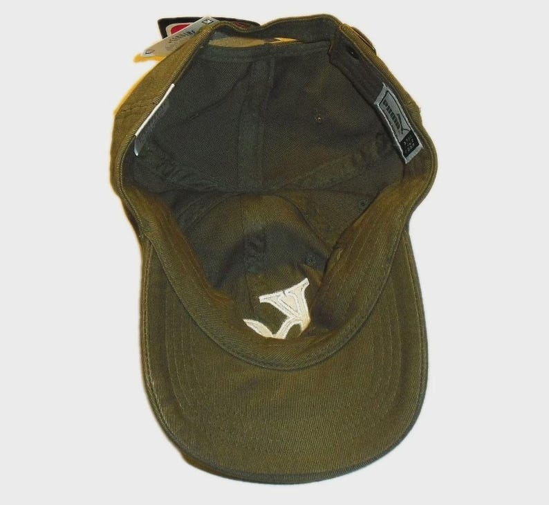 May include: An olive green baseball cap shown from an interior perspective, revealing the fabric lining, a white embroidered logo on the inner crown, and a rectangular brand tag attached to the inner seam near the back opening of the headwear.