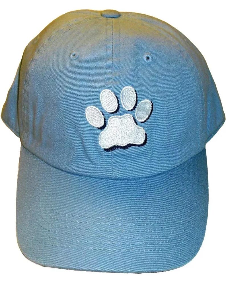 Pu&ograve; includere: Un berretto da baseball blu chiaro con un'impronta di zampa bianca ricamata sul davanti.