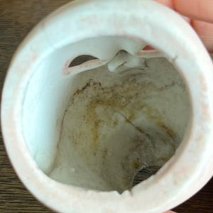 May include: A close-up view of the inside of a white porcelain doll head. The interior shows a hollow space with a crack and discoloration. The rim of the head is a soft pink color.