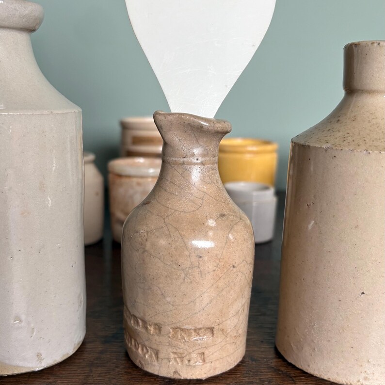May include: A collection of small, vintage, ceramic bottles with a crackled glaze. The bottles are various shades of beige and cream. One bottle is in focus and has the text "HORNSBY & SONS LTD" embossed on the side.