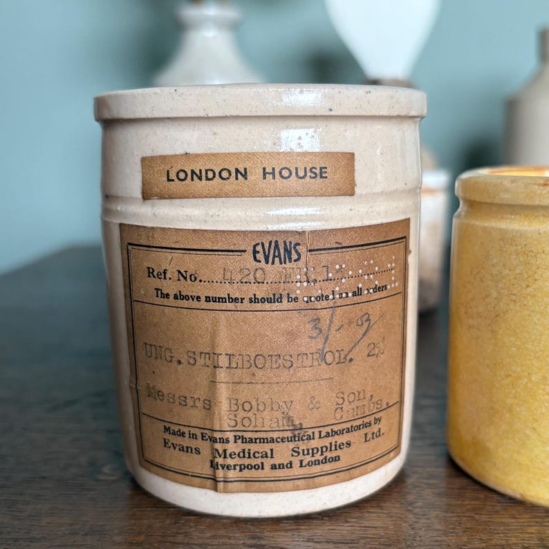 May include: A white ceramic jar with a brown label that reads "LONDON HOUSE EVANS Ref. No. 420 The above number should be quoted in all orders. 3/93 UNG. STILBOESTROL. 2% Messrs Bobby & Sons. Sohalt Cambs Made in Evans Pharmaceutical Laboratories by Evans Medical Supplies Ltd. Liverpool and London"