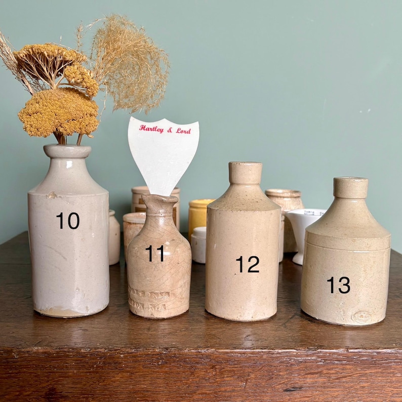 May include: Five vintage stoneware bottles with cork tops. The bottles are numbered 10, 11, 12, and 13. The bottles are all different sizes and shapes. The bottles are on a wooden table.