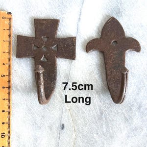 Puede incluir: Dos ganchos rústicos de metal, uno con forma de cruz y el otro con forma de flor de lis. Ambos ganchos miden 7,5 cm de largo y tienen un acabado marrón oscuro.