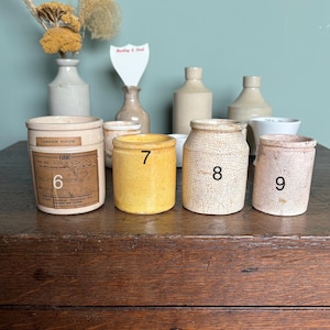 May include: Six vintage ceramic jars with labels and numbers 6, 7, 8, and 9. The jars are on a wooden surface.