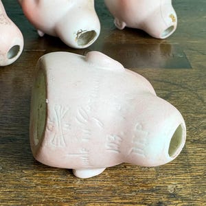 May include: Several antique porcelain doll heads in various stages of wear. The heads are a pale pink color with visible facial features and open neck holes. Some show signs of age and wear, with chipped paint and discoloration.