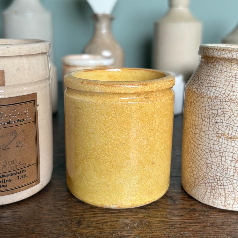 May include: A yellow ceramic jar with a wide mouth and a smooth, slightly textured surface. The jar is sitting on a wooden surface.