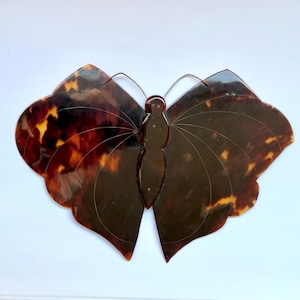 Puede incluir: Un broche de mariposa de carey marrón y negro con un diseño detallado. Las alas están talladas de forma intrincada y el cuerpo está esculpido con un diseño en relieve.