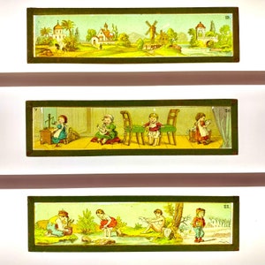 May include: Three antique magic lantern slides with hand-painted scenes. The top slide depicts a rural landscape with a windmill. The middle slide shows children in domestic settings. The bottom slide shows children playing outdoors. Each slide is framed in green.