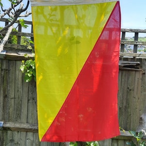 Puede incluir: Una bandera amarilla y roja con una línea diagonal que divide los colores. La bandera está colgada de una cuerda.