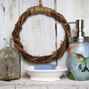 May include: A bathroom decor set with a glass bottle, a soap dispenser with a hummingbird design, and a soap dish with a bar of soap. The soap dispenser is made from a repurposed mason jar with a stainless steel pump.