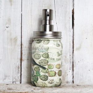 May include: A white glass soap dispenser with a silver pump top. The dispenser has a floral design with birds and the text "Fleur-Toujours" and "From the Garden".