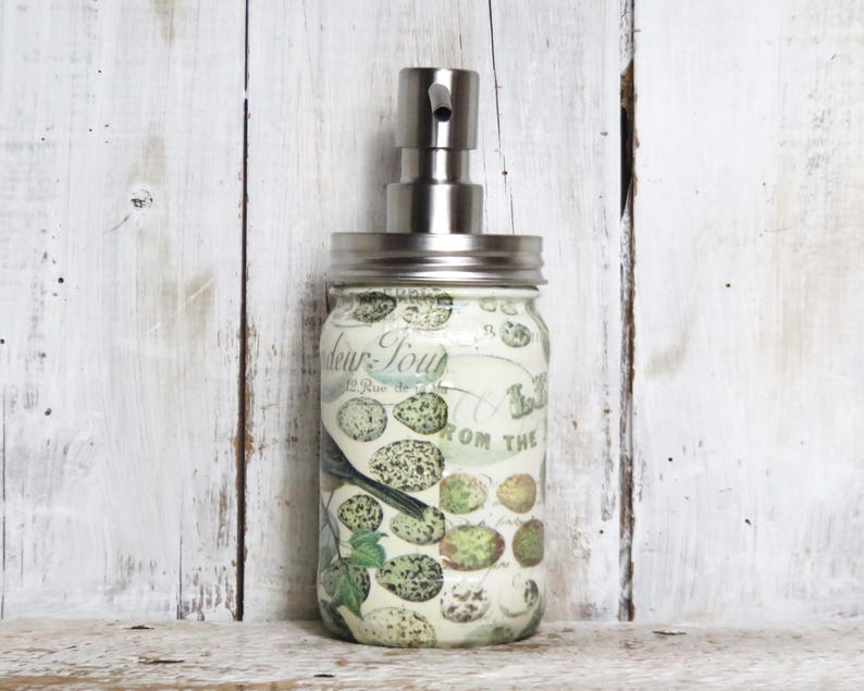 May include: A white glass soap dispenser with a silver pump top. The dispenser has a floral design with birds and the text "Fleur-Toujours" and "From the Garden".