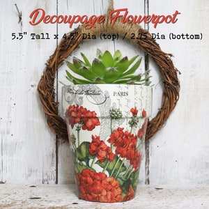 May include: A white ceramic flowerpot with a floral design featuring red flowers and green leaves. The pot is 5.5 inches tall, 4.5 inches in diameter at the top, and 2.75 inches in diameter at the bottom. The pot is decorated with a decoupage technique and has the word "PARIS" printed on it.