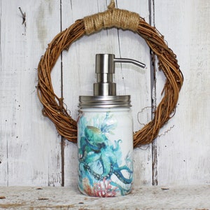 May include: A white glass soap dispenser with a stainless steel pump and lid. The dispenser is decorated with a blue and green octopus and coral design.