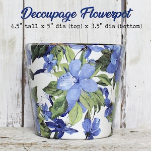 May include: A white ceramic flowerpot with a decoupage design of blue and green flowers. The pot is 4.5 inches tall, 5 inches in diameter at the top, and 3.5 inches in diameter at the bottom.
