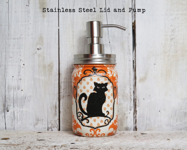 May include: Orange and white mason jar soap dispenser with a black cat design and a stainless steel lid and pump. "Stainless Steel Lid and Pump" is written above the jar.