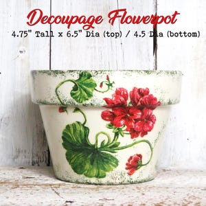 May include: White ceramic flowerpot with a decoupage design of red flowers and green leaves. The pot is 4.75 inches tall, 6.5 inches in diameter at the top, and 4.5 inches in diameter at the bottom.
