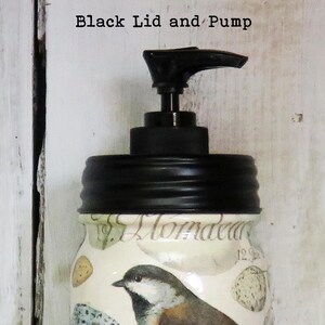 May include: A glass jar with a black lid and pump. The jar has a floral design with a bird on it. The text "Almada" is visible on the jar.