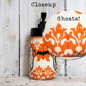 May include: A white mason jar with a black pump top and a black lid. The jar is decorated with an orange and white damask pattern with black bats and ghosts. The text "Ghosts!" is written in black on the jar.
