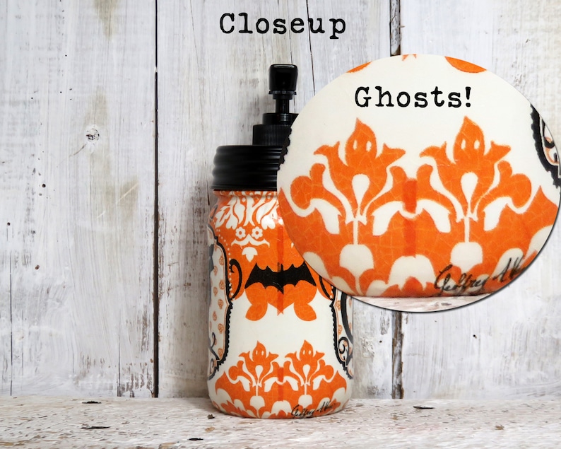 May include: A white mason jar with a black pump top and a black lid. The jar is decorated with an orange and white damask pattern with black bats and ghosts. The text "Ghosts!" is written in black on the jar.