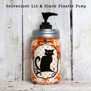 May include: Orange and white Halloween themed glass jar with a black cat design and a black plastic pump dispenser. The jar has a galvanized metal lid.