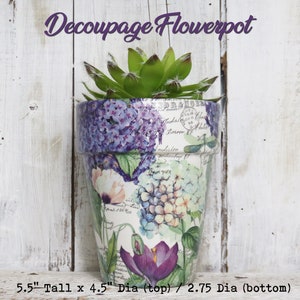 May include: A white ceramic flowerpot with a decoupage design featuring purple, pink, and green flowers. The pot is 5.5 inches tall, 4.5 inches in diameter at the top, and 2.75 inches in diameter at the bottom.