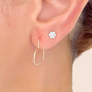 Puede incluir: Un par de pendientes de oro, uno es un pequeño pendiente de flor con piedras de circonita cúbica transparentes, el otro es un pendiente de aro simple.