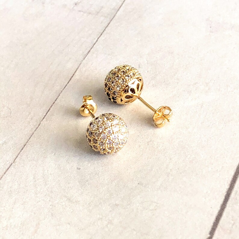 A pair of gold cz ball stud earrings with a round, sparkly design. The earrings are made of gold and have a clear, sparkly stone.