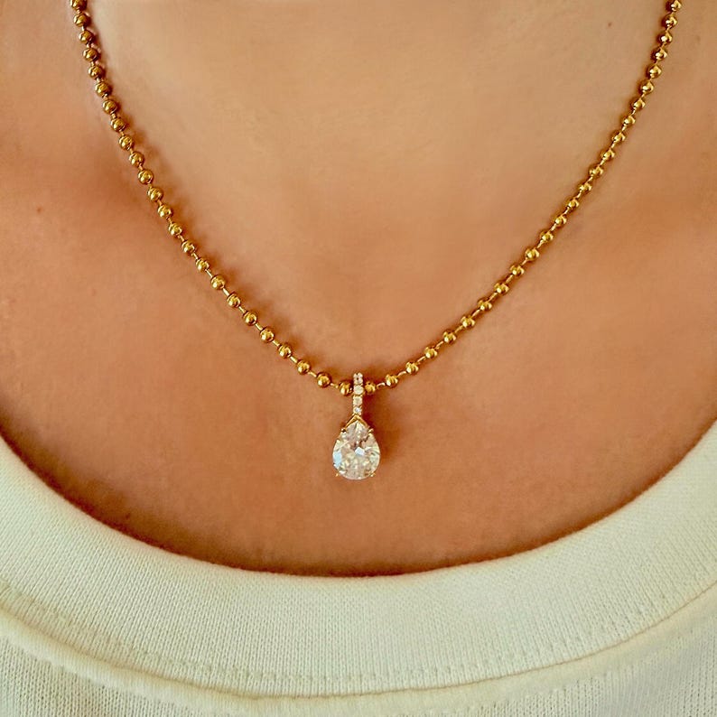 Close-up of pear shaped CZ pendant resting on collarbone on 18K PVD gold 3mm ball chain showing warm yellow gold tone and teardrop cubic zirconia detail