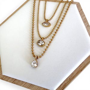 Three 18K PVD gold CZ pendant necklaces worn layered showing oval marquise and pear styles together adjustable from 16 to 18 inches