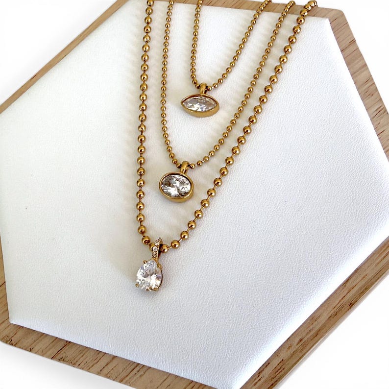 Three 18K PVD gold CZ pendant necklaces worn layered showing oval marquise and pear styles together adjustable from 16 to 18 inches