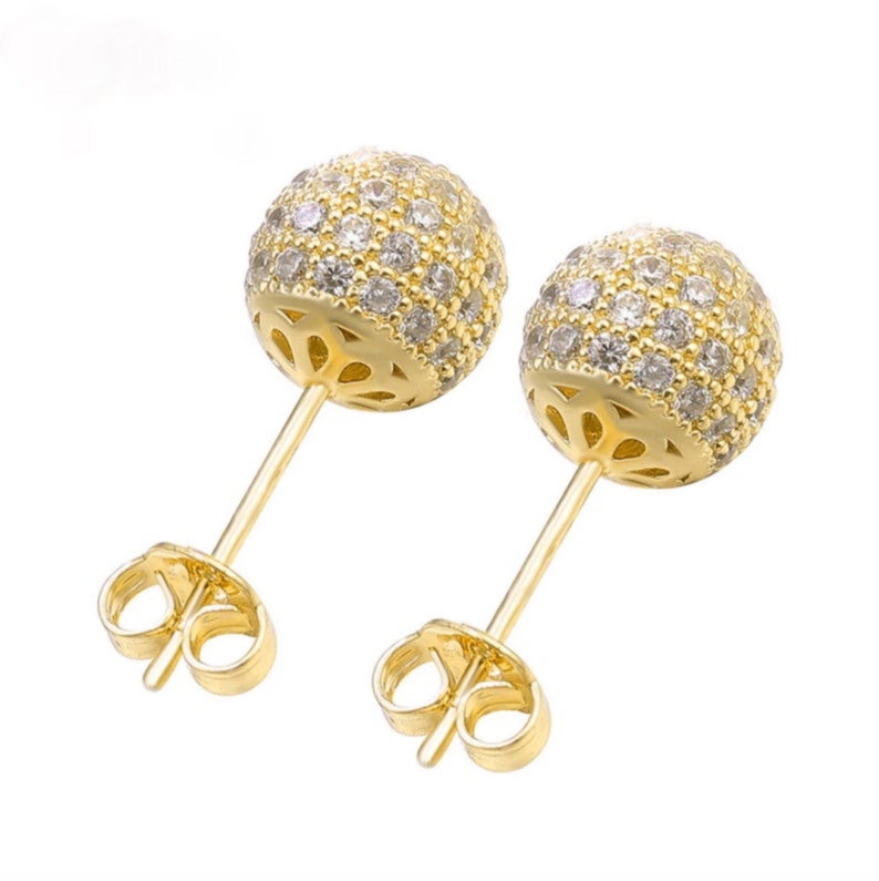 Close up of a pair of gold stud earrings with a round, clear crystal design. The earrings have a post and butterfly back.