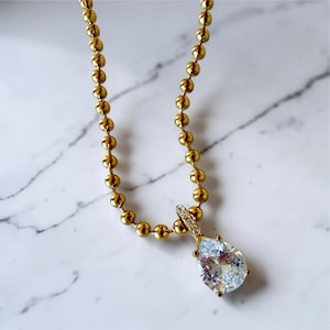 Close up of Pear cubic zirconia teardrop pendant necklace on white marble showing 18K PVD gold 3mm ball chain with pavé bail and sparkling CZ stone