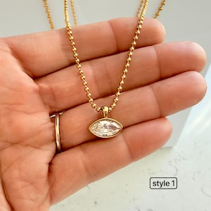 Close-up of marquise cubic zirconia pendant on 18K PVD gold 2mm ball chain held in palm showing warm yellow gold tone and sparkling CZ stone detail