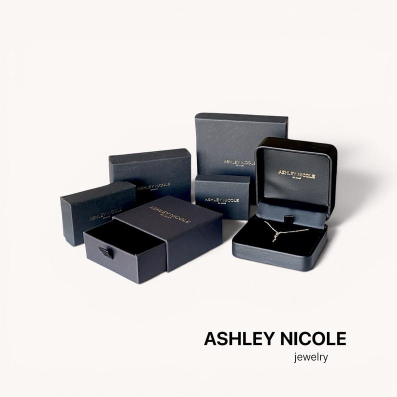 May include: An assortment of black jewelry boxes, some open to reveal a necklace. The boxes are various sizes and shapes, with the brand name "ASHLEY NICOLE" printed on them. The word "jewelry" is below the brand name.