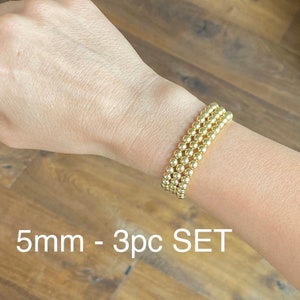 May include: A set of three gold beaded bracelets, each with 5mm beads. The bracelets are stacked on a person's wrist. 5mm - 3pc SET
