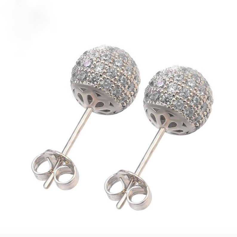 Close up of a pair of silver stud earrings with a round, clear crystal design. The earrings have a post and butterfly back.