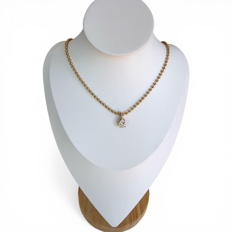 Pear cubic zirconia teardrop pendant necklace on white jewelry bust showing 18K PVD gold 3mm ball chain with pavé bail and sparkling CZ stone