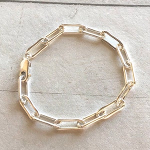May include: A silver chain bracelet with a link style that resembles paper clips. The bracelet is made of a polished metal and has a simple, modern design.