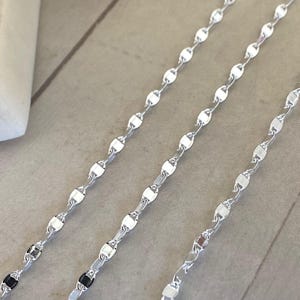 May include: Three silver chains with a delicate oval link design. The chains are laid out in a row on a light grey surface.